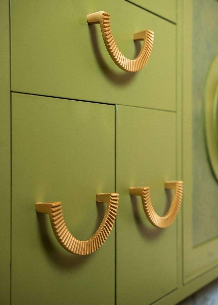 Three gold cup pulls on a green cabinet with paneled doors
