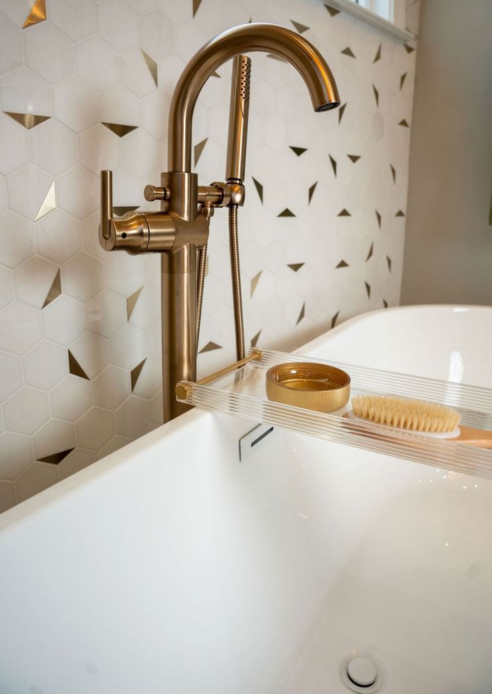 Gold faucet over a white bathroom sink with patterned tile backsplash