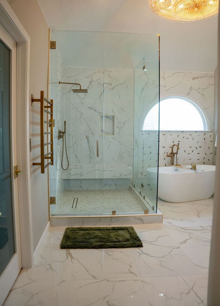 Modern bathroom with glass shower, marble tiles, freestanding tub, and green bath mat