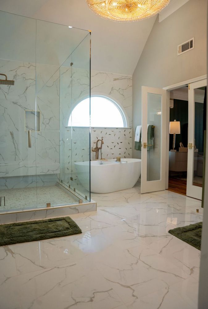Luxurious white marble bathroom with glass shower, soaking tub, and chandelier under a vaulted ceiling