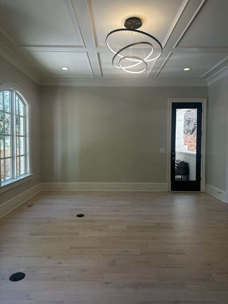 Empty modern room with light wood floors, white walls, a ceiling light, and windows on two sides.