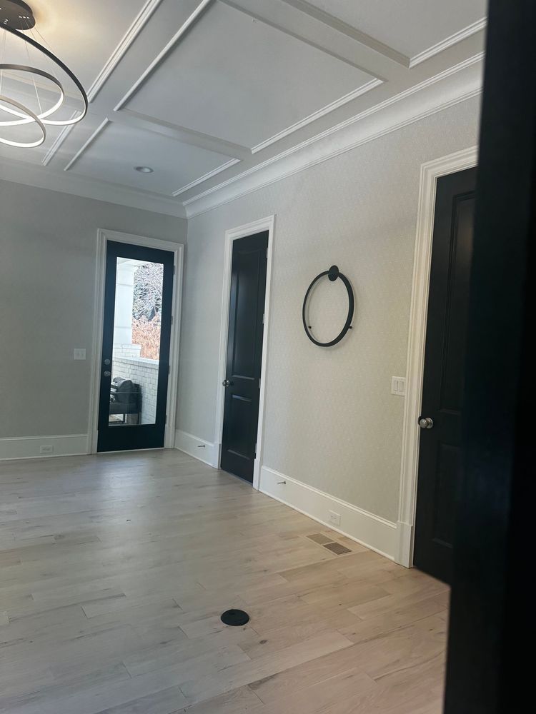Empty modern room with light wood floors, gray walls, black doors, and a round wall mirror.