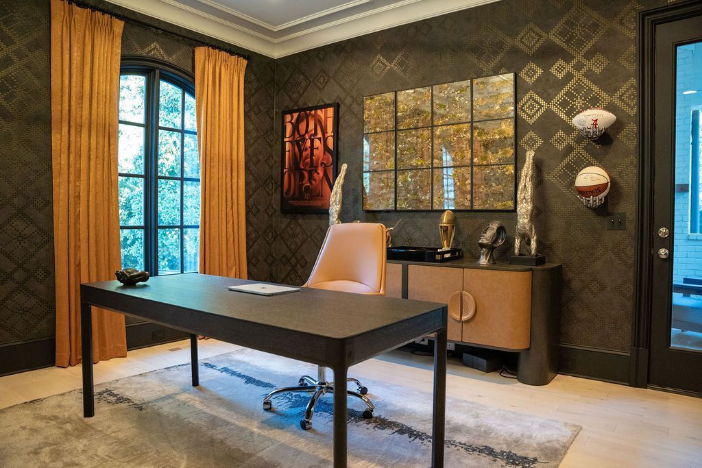 Modern office with a black desk, tan chair, patterned wallpaper, and tall windows.