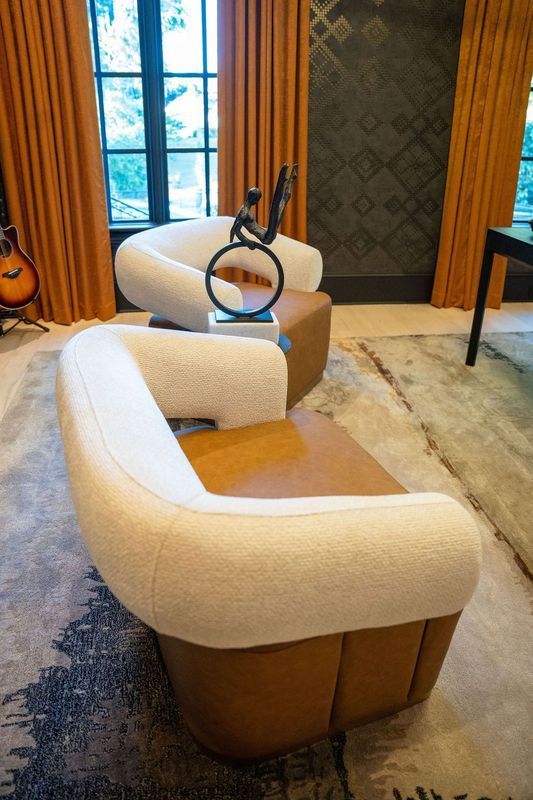 Modern lounge with two cream and tan armchairs, a guitar, window, patterned wall, and rug.