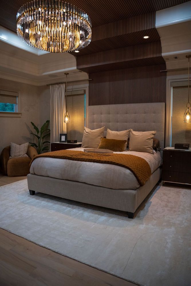 Elegant bedroom with a beige upholstered bed, chandelier, warm lighting, and neutral decor