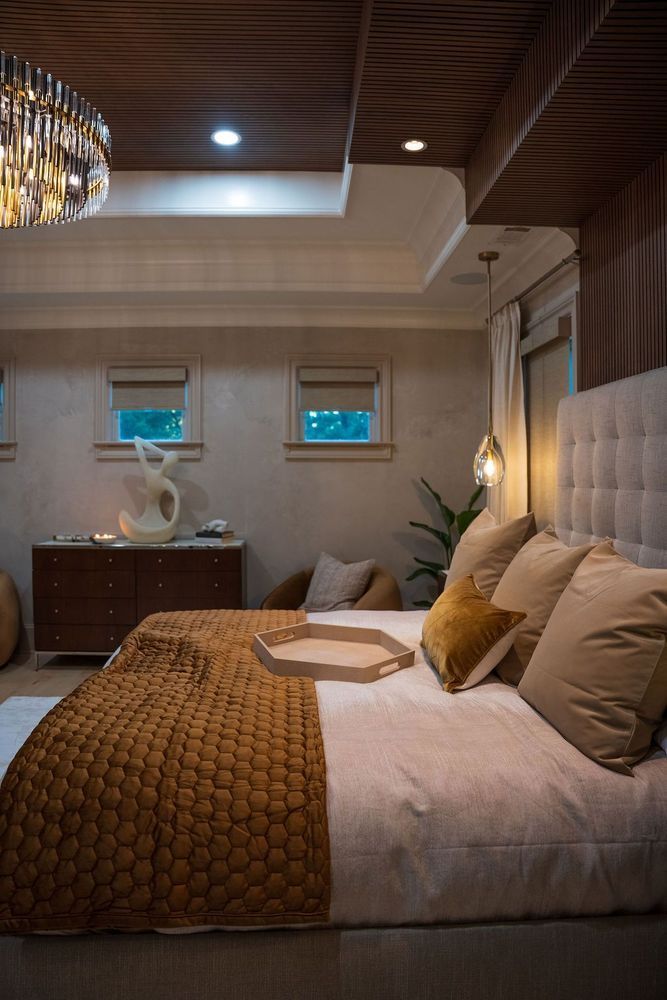 Cozy bedroom with tufted headboard, beige bedding, wood ceiling, chandelier, and two small windows.
