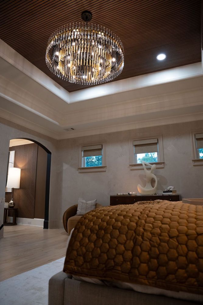 Elegant bedroom with crystal chandelier, arched doorway, and warm-toned tufted bedspread