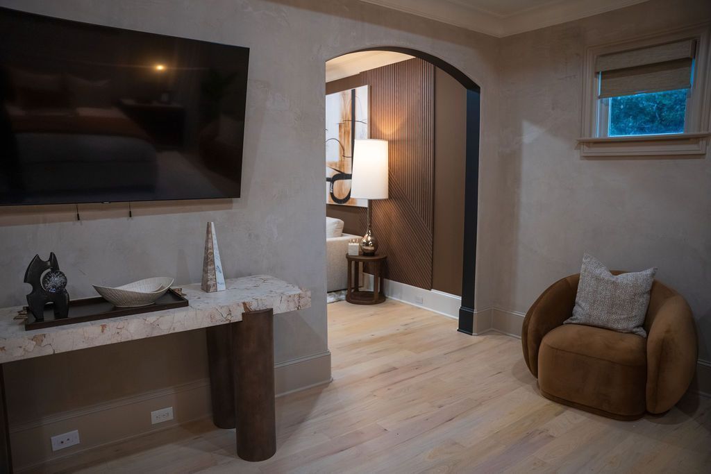 Modern living room with wall-mounted TV, arched doorway, tan chair, and small window seat