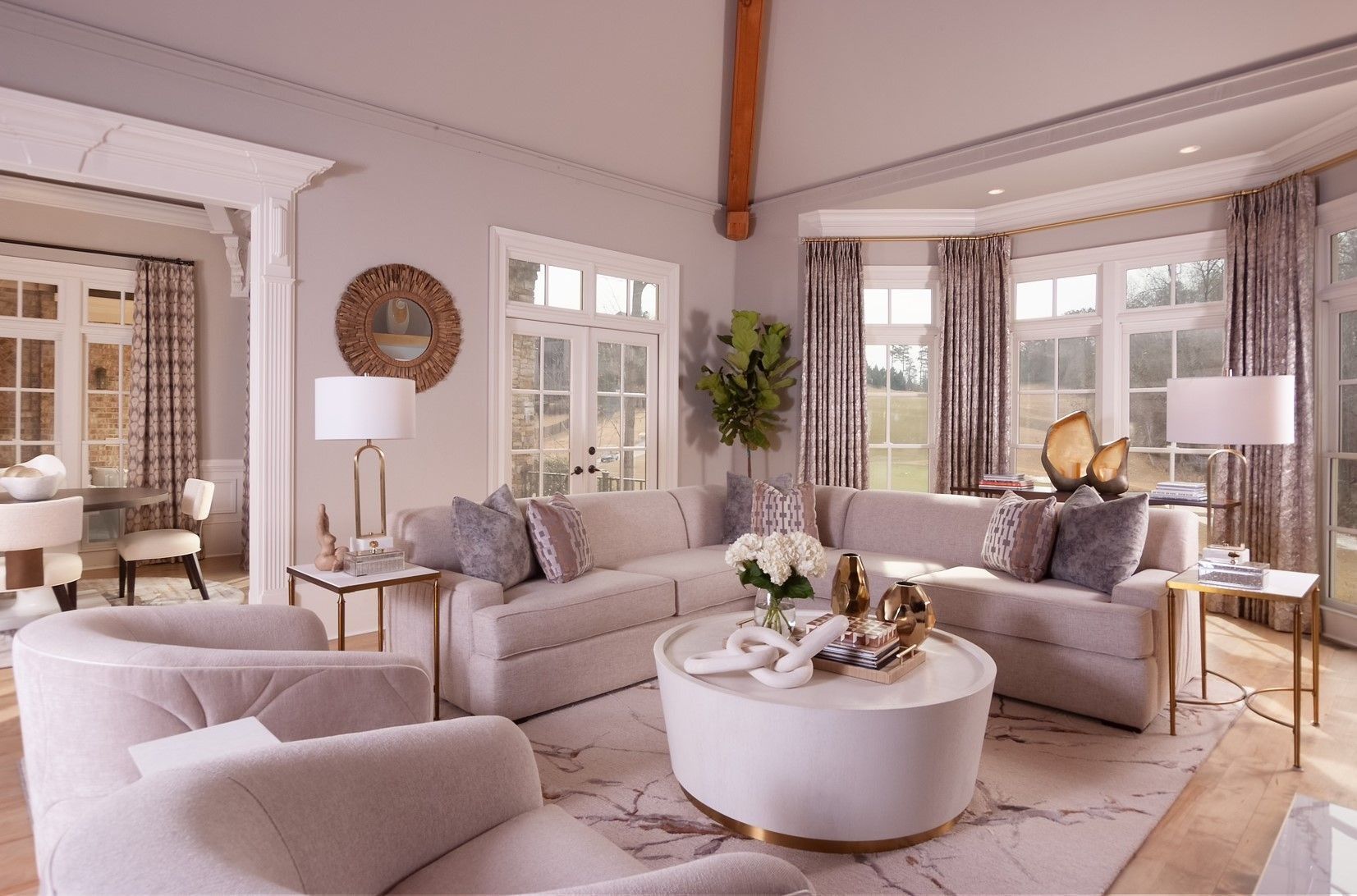 Elegant beige living room with curved sofa, round coffee table, lamps, and large windows with curtains