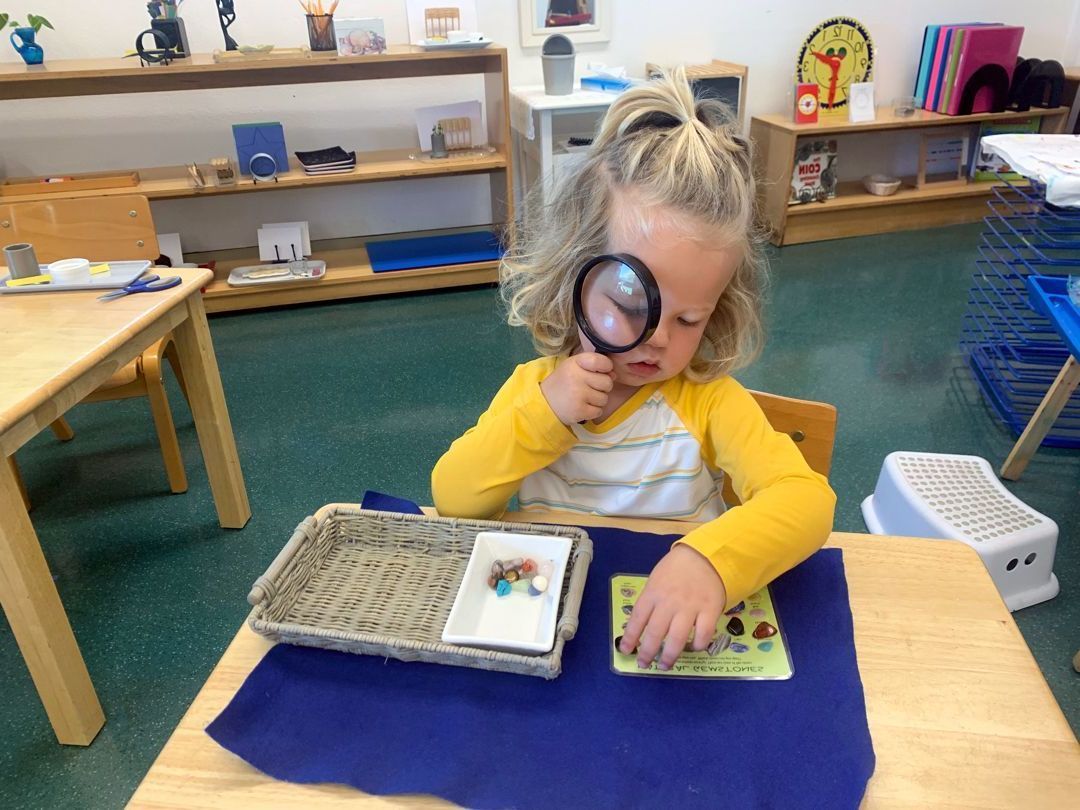 A Montessori child looking at rocks with a magnifying glass.