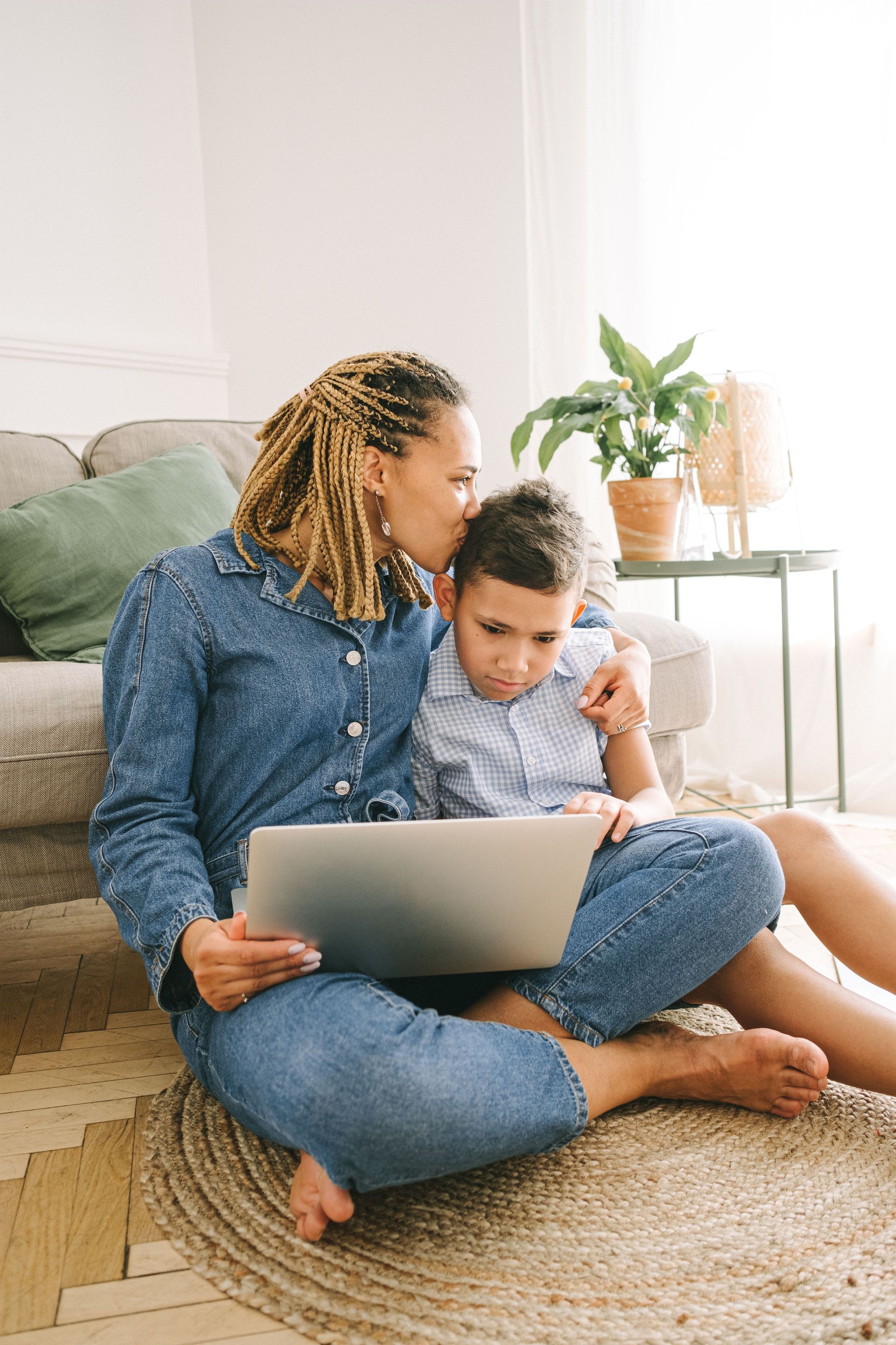 Adult and child sitting on a rug using a laptop in a bright living room