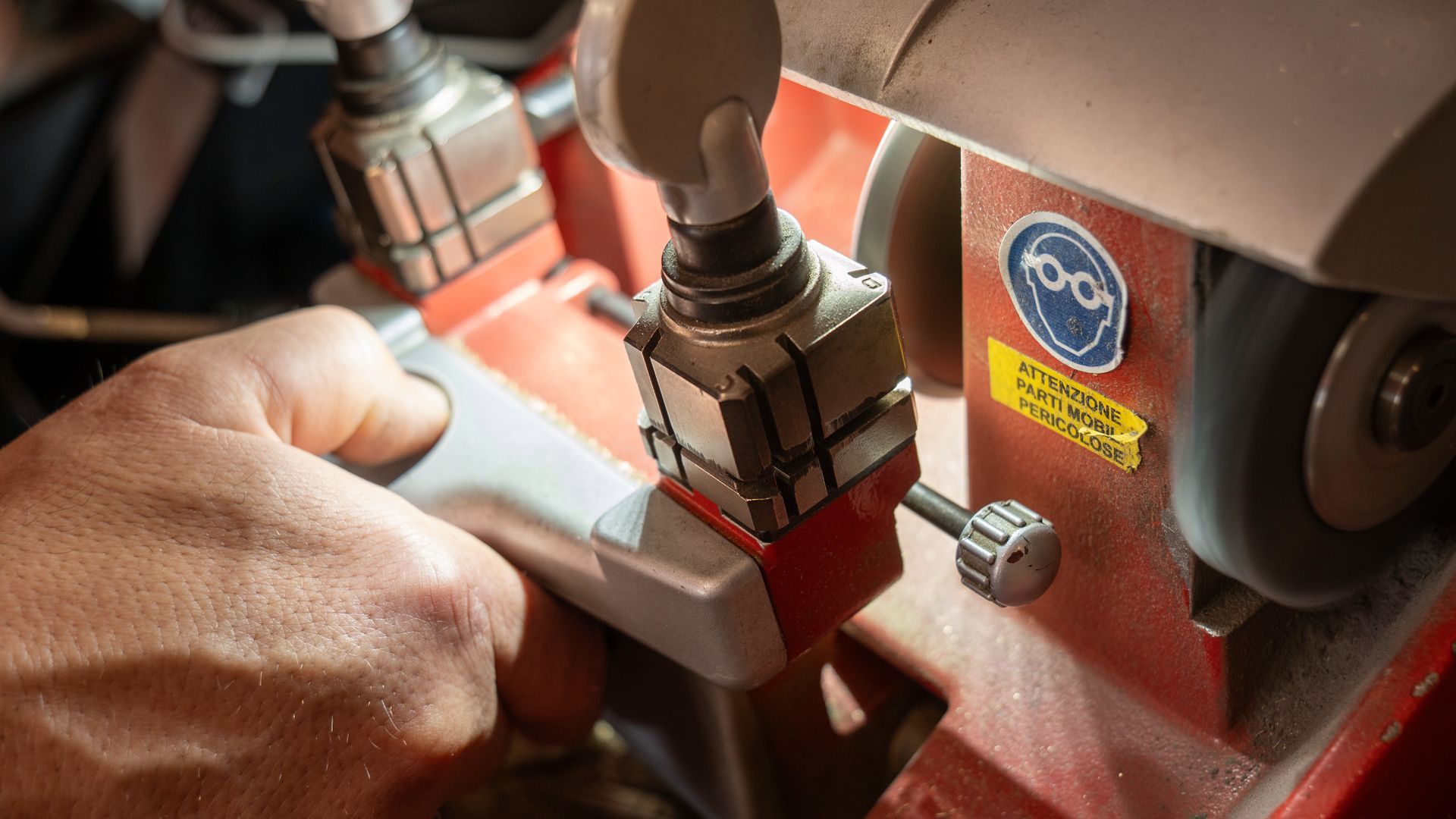 Regolazione manuale di una piccola macchina industriale rossa con componenti metallici e un'etichetta con logo blu.