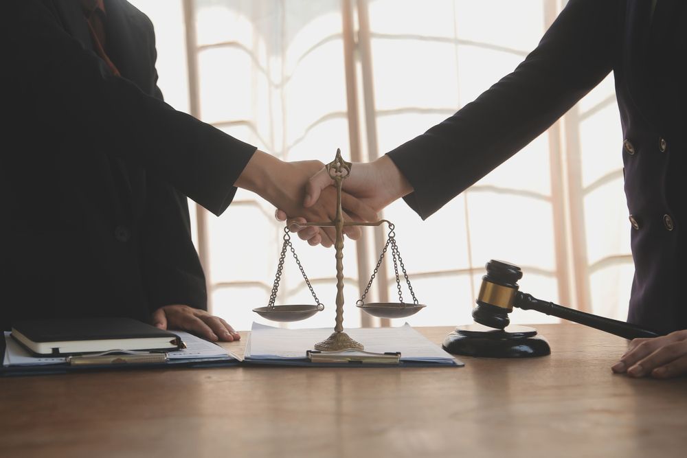 A judge and a lawyer are shaking hands in front of a scale of justice.