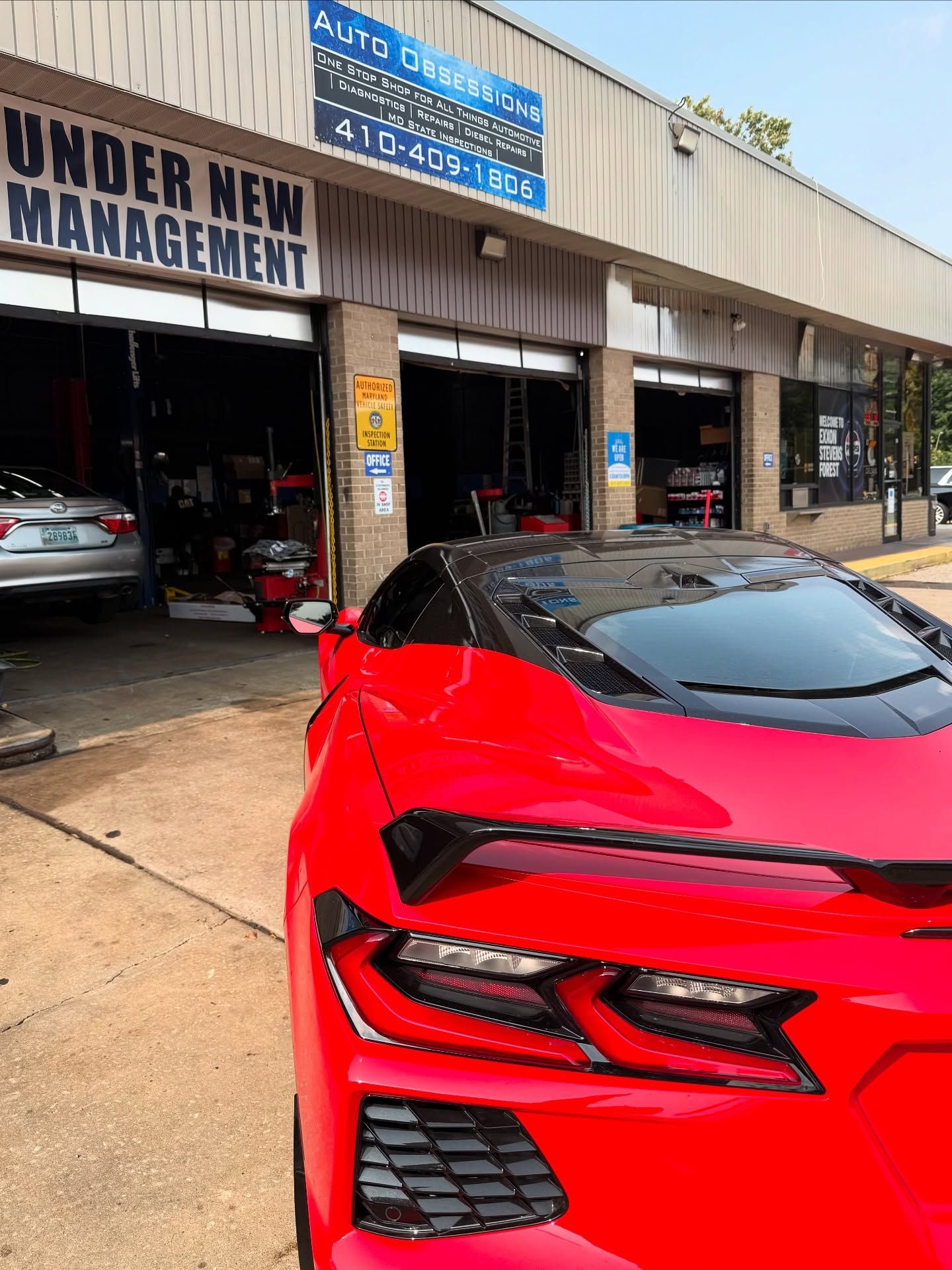 Red sports car parked outside an auto shop with an “Under New Management” sign. | Auto Obsessions Auto Repair