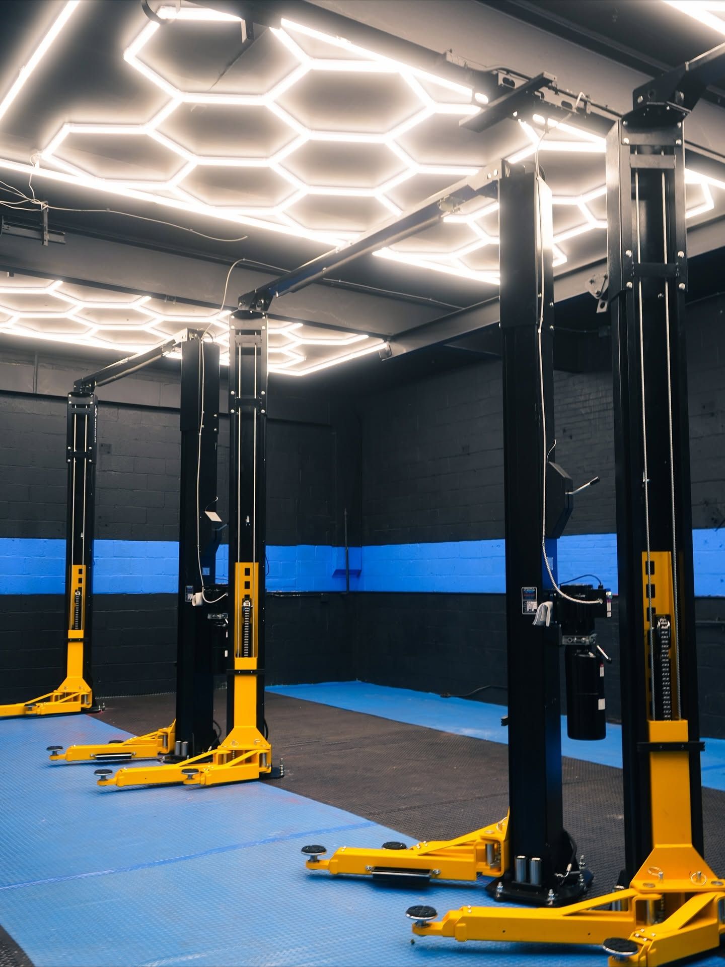 Modern gym with yellow-and-black training rigs and hexagonal LED ceiling lights | Auto Obsessions Auto Repair