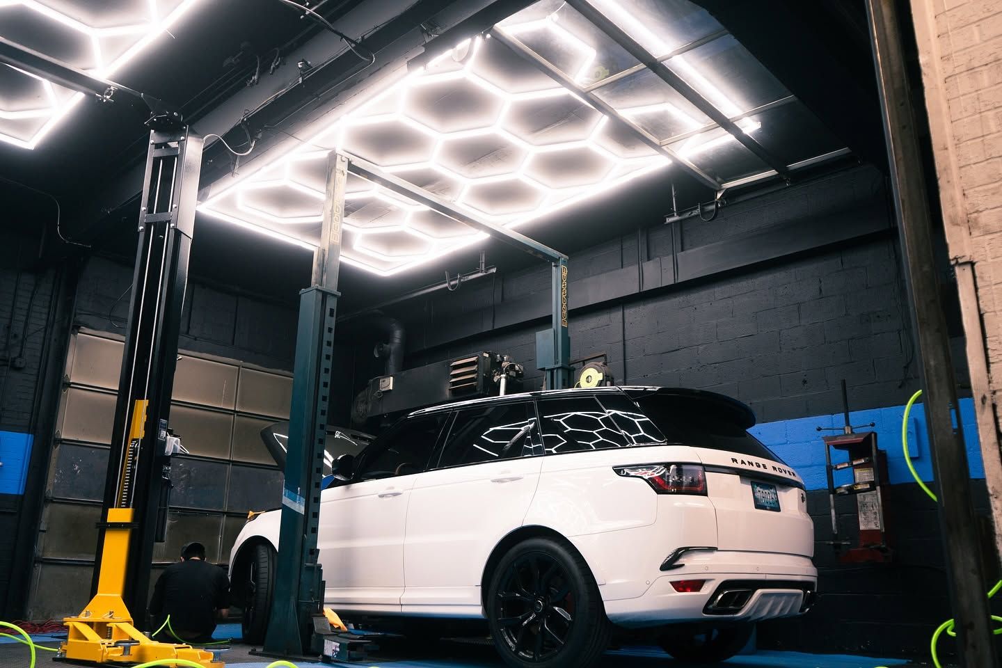 White SUV in a car wash bay under bright overhead lights, with water hoses and cleaning equipment nearby  | Auto Obsessions Auto Repair