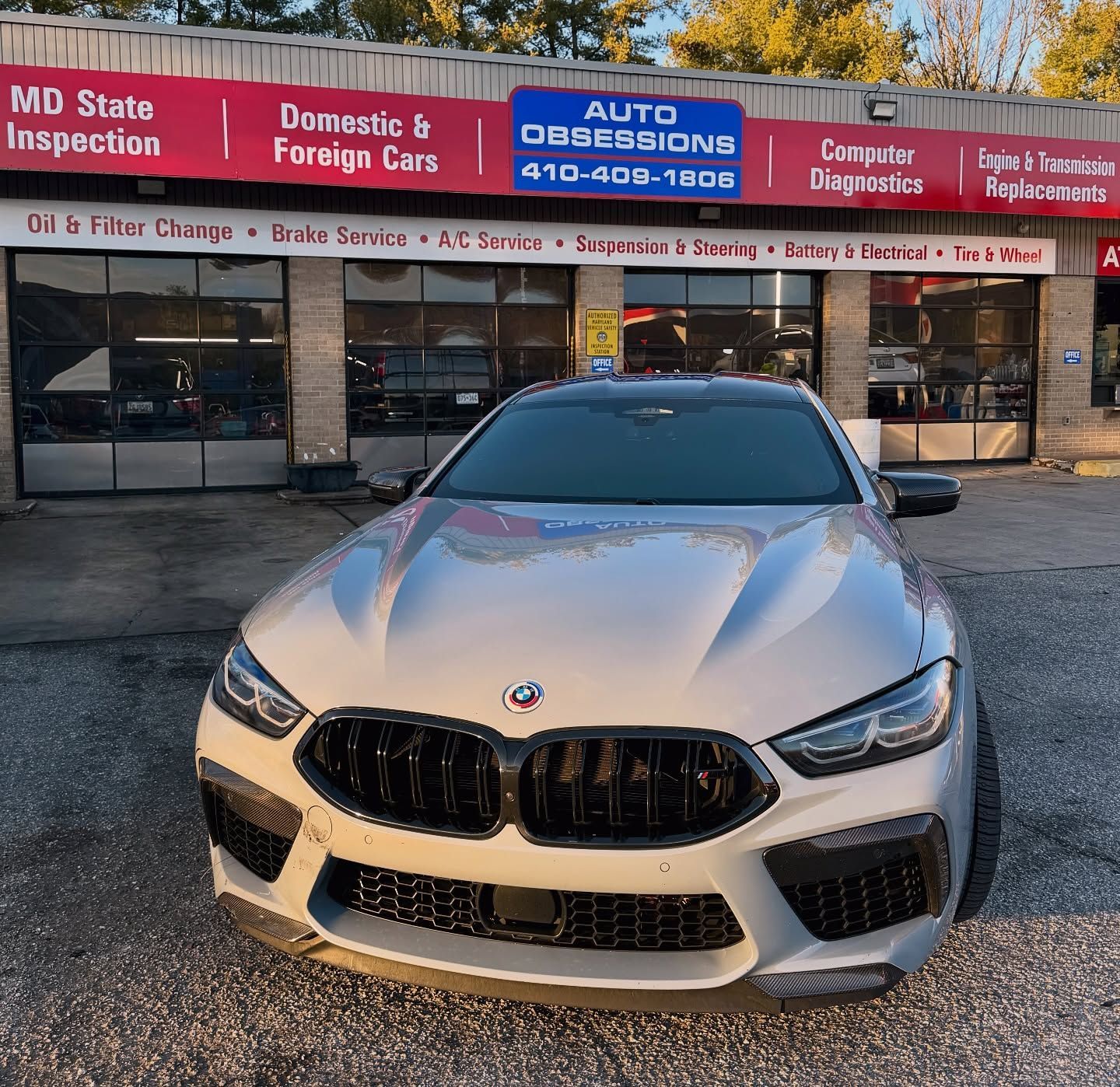 White BMW coupe parked in front of an auto service shop with red and blue signage | Auto Obsessions Auto Repair