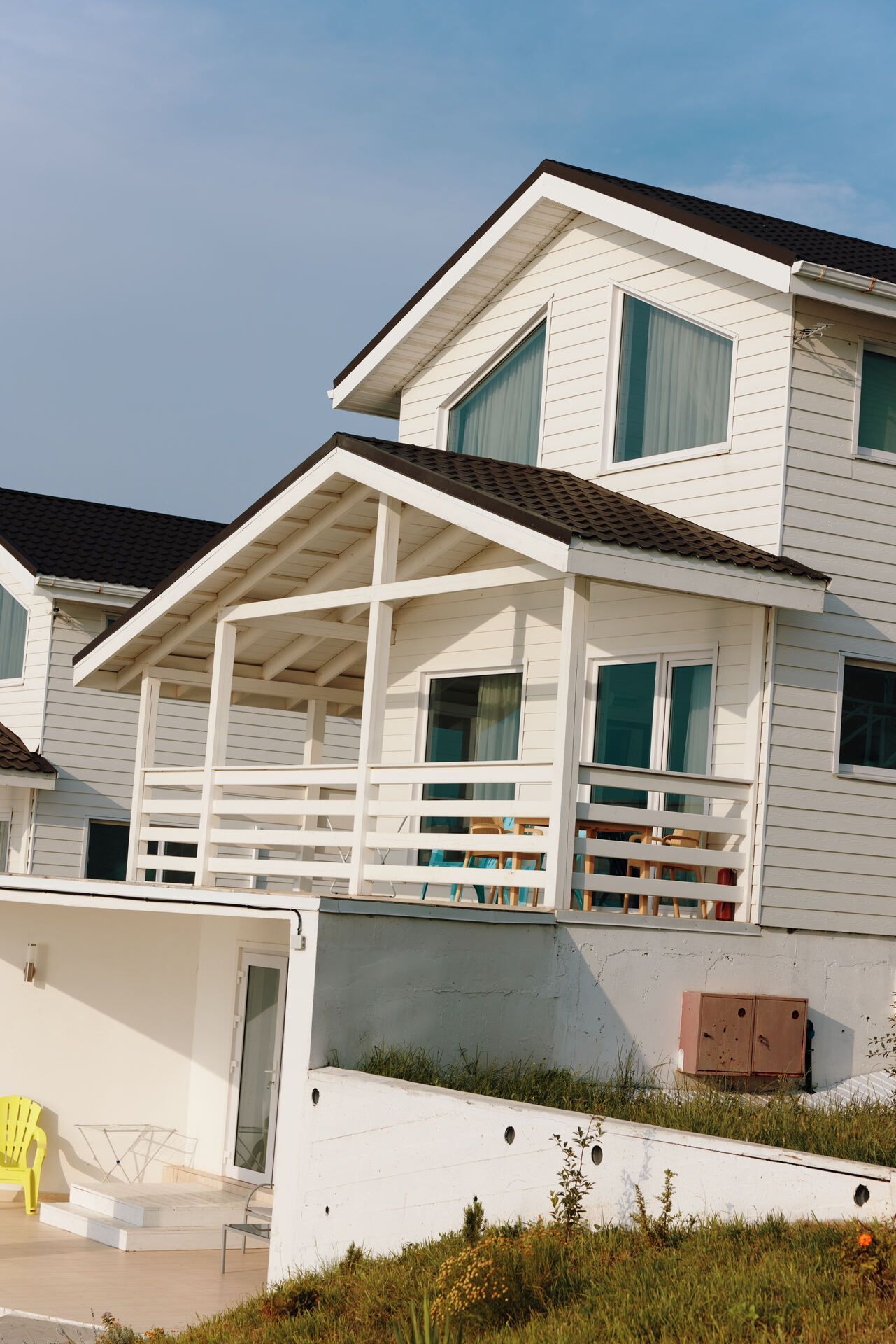White two-story house with a covered porch and teal window shutters under a blue sky