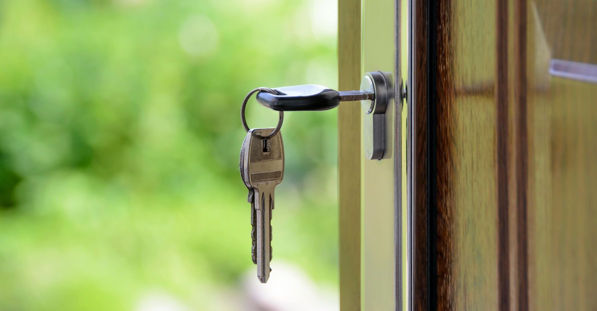 Keys hanging in a door lock on a wooden door with a blurred green background