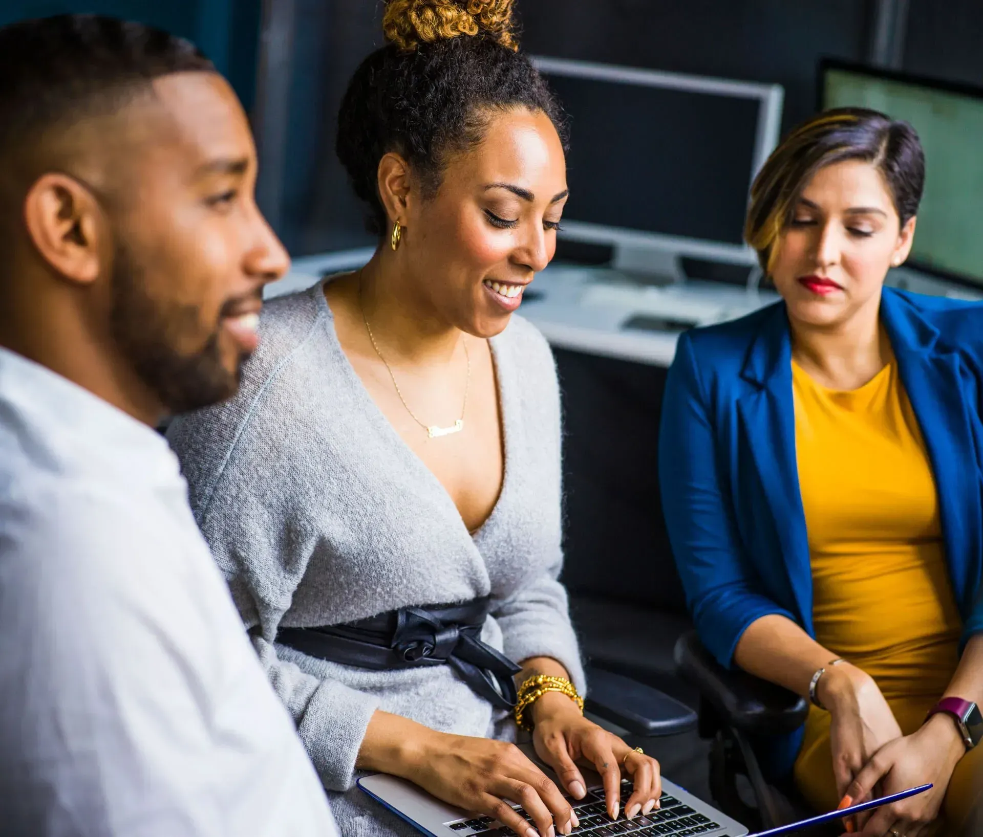Three coworkers in a meeting, smiling and looking at a laptop in an office setting