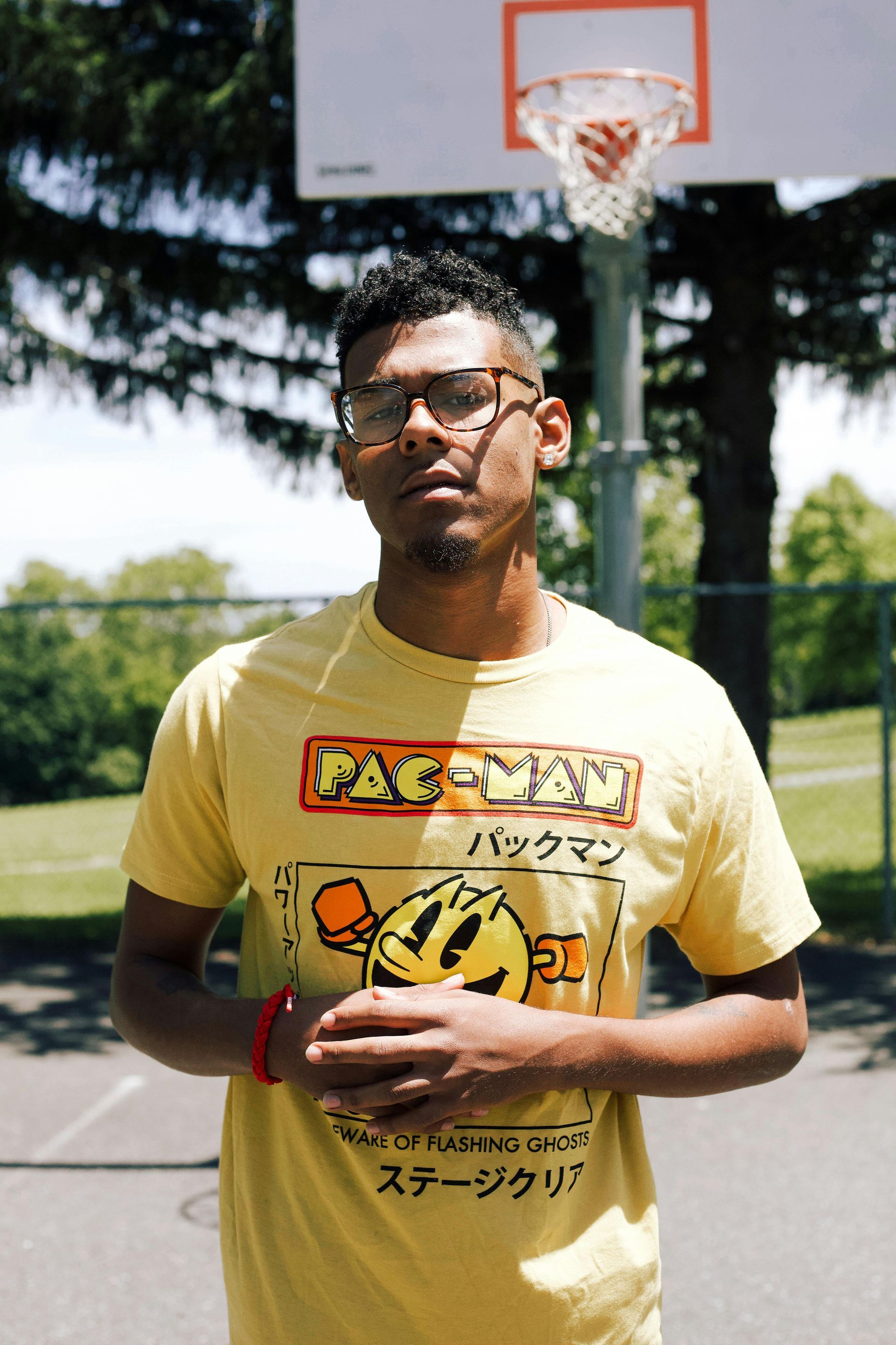 Person standing on an outdoor basketball court holding a basketball, with a hoop behind them.
