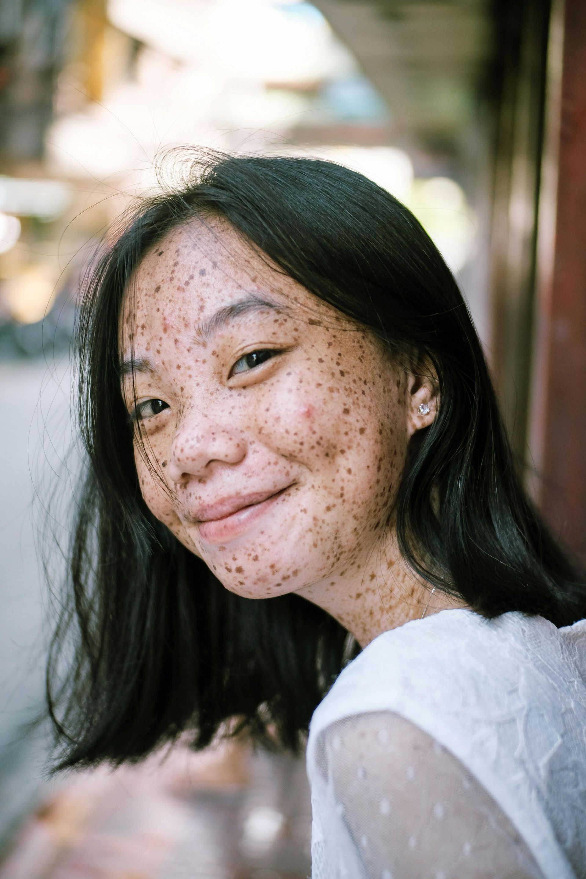 Close-up portrait of a smiling person with dark hair in a softly blurred outdoor setting