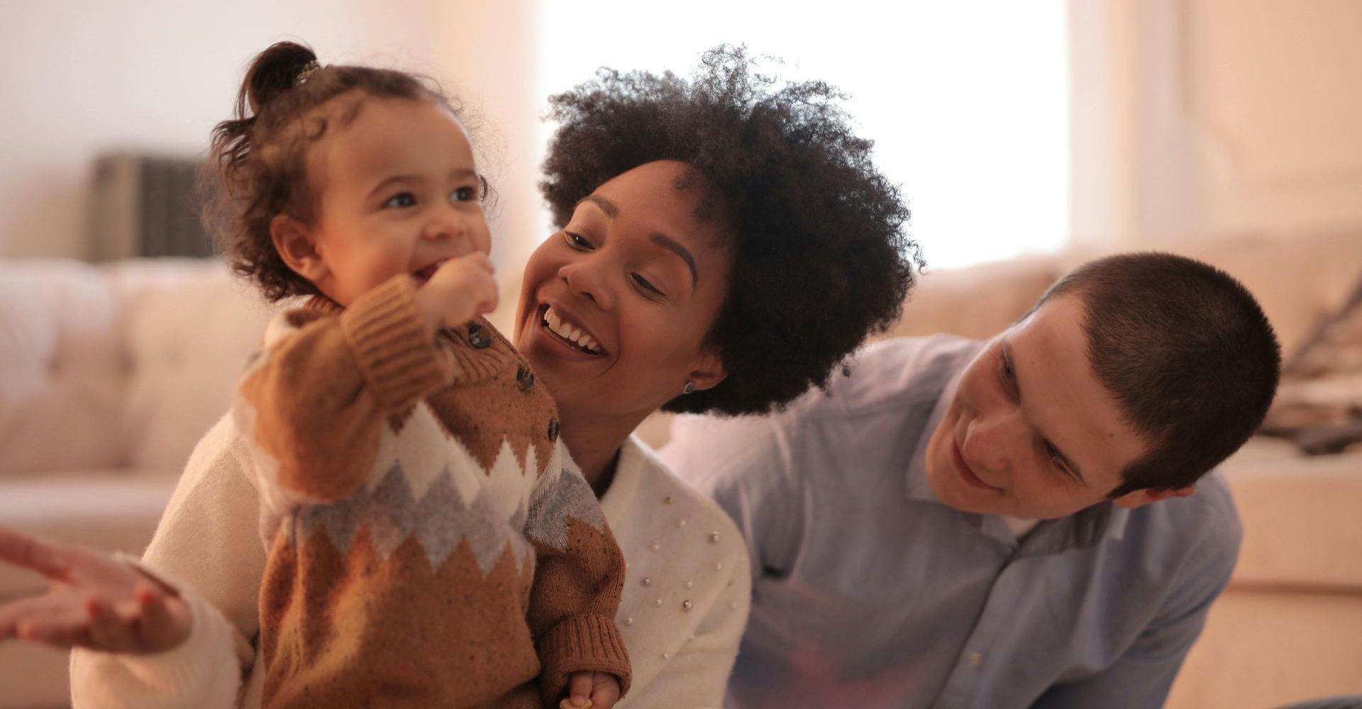 Smiling family on a couch, with a child in a brown sweater and two adults leaning in close.