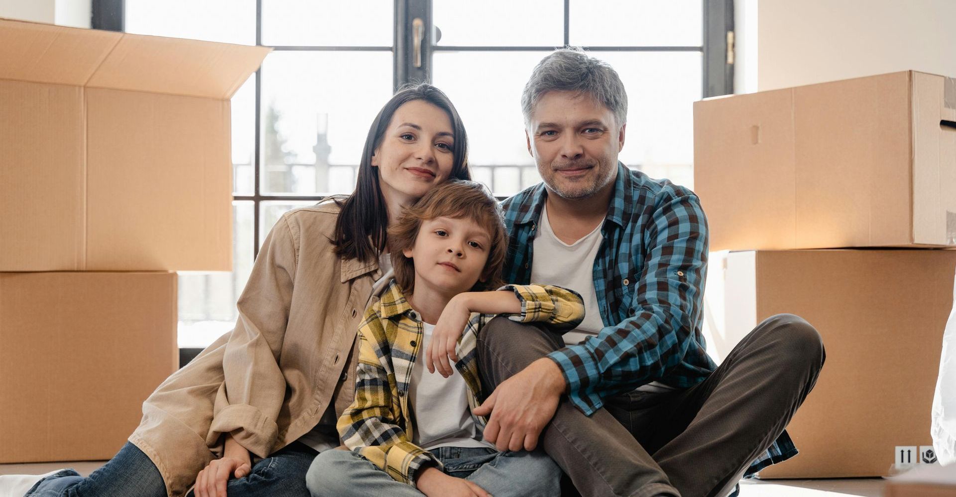 Family sitting among moving boxes in a bright room, smiling at the camera.