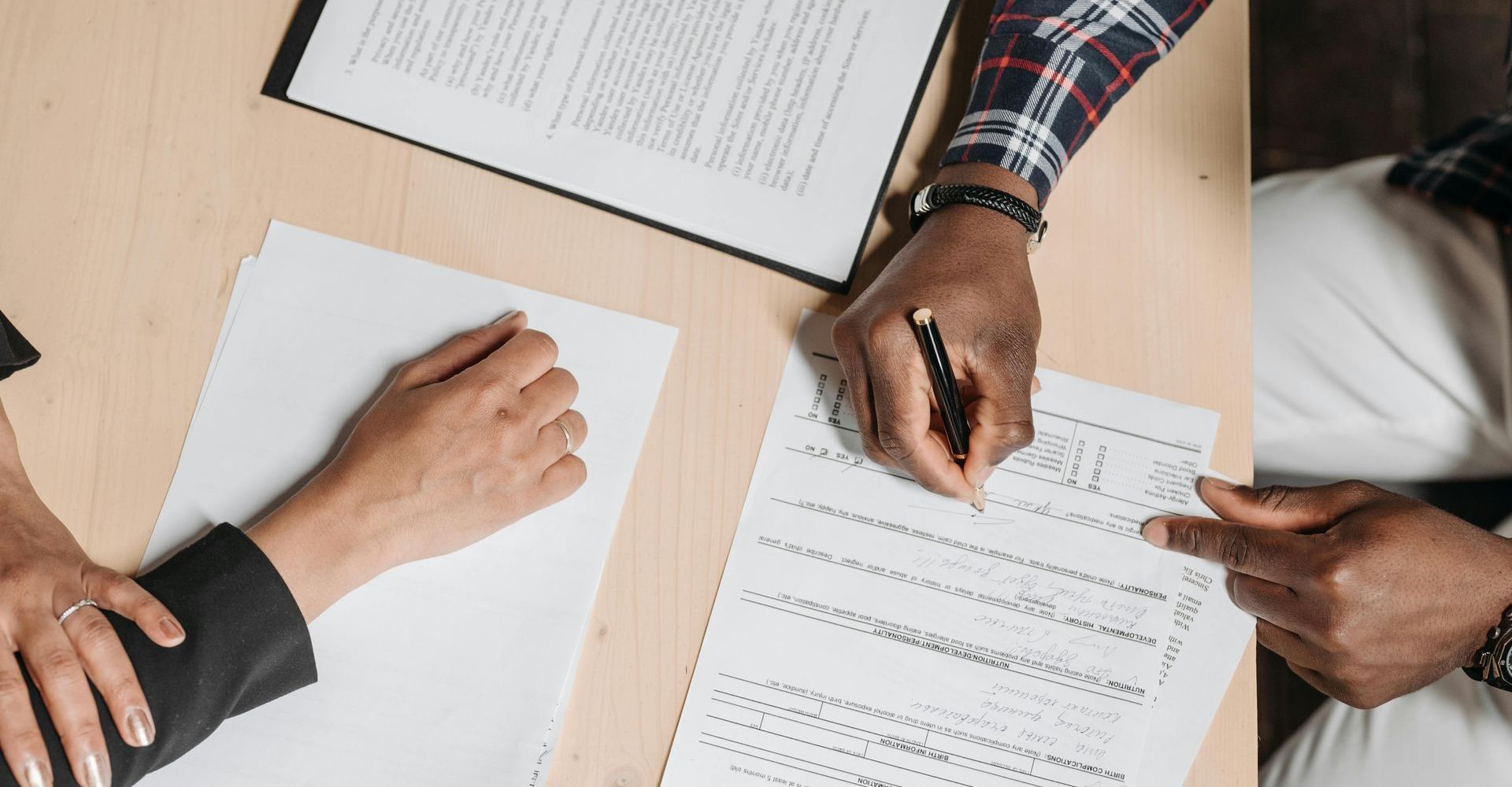 Hands reviewing and signing documents around a wooden table.