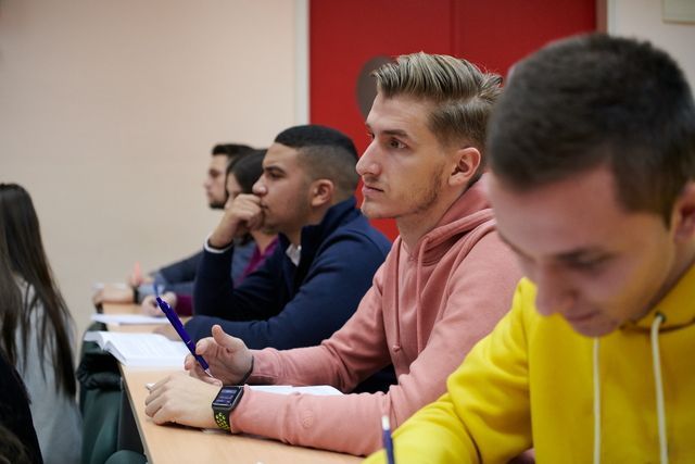 Students seated in a classroom, taking notes during a lecture.