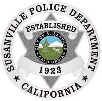 The Susanville Police department patch is a blue shield featuring a central circular logo of a tree, deer, and mountains.
