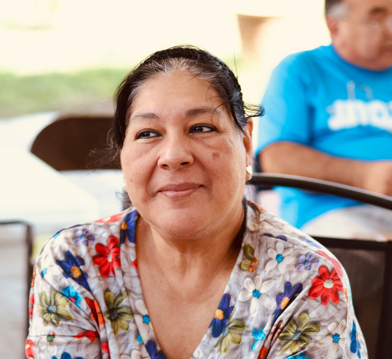 A person with dark hair wearing a white shirt with a multicolored floral pattern, looking slightly away from the camera.