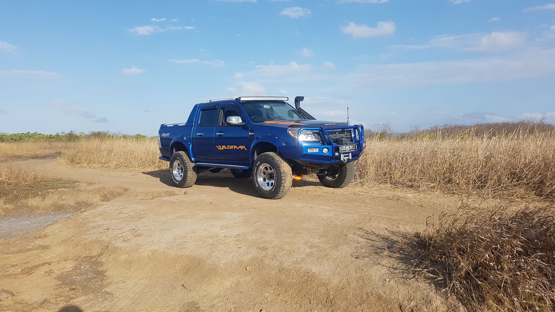Blue Off-Road Truck Driving on A Dirt Path Beside Dry Grass — Ironhide Customs In Garbutt, QLD