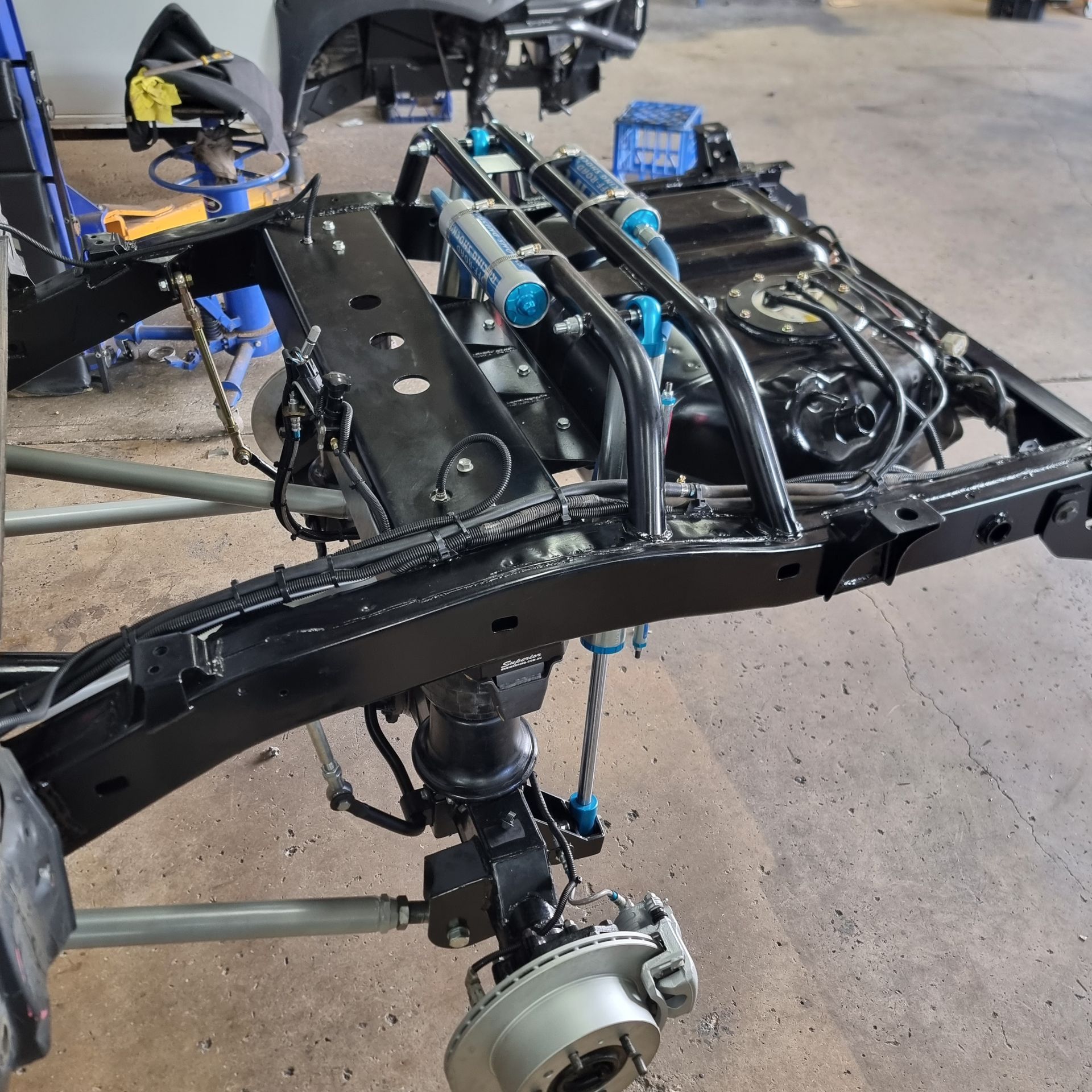 A Black Truck Chassis in A Shop with Custom Blue Suspension — Ironhide Customs In Garbutt, QLD