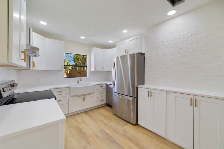 White kitchen with stainless steel appliances, light wood floor, and white cabinets.
