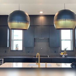 Modern kitchen with black cabinets, gold fixtures, white countertops, and two gold-rimmed pendant lights.