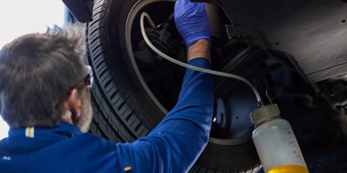 Mechanic inspecting a vehicle wheel undercarriage with a tool and spray bottle in a garage