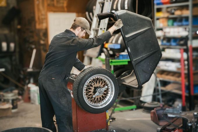 Mechanic lifting a car on a hydraulic jack in a garage, with a wheel visible in the foreground
