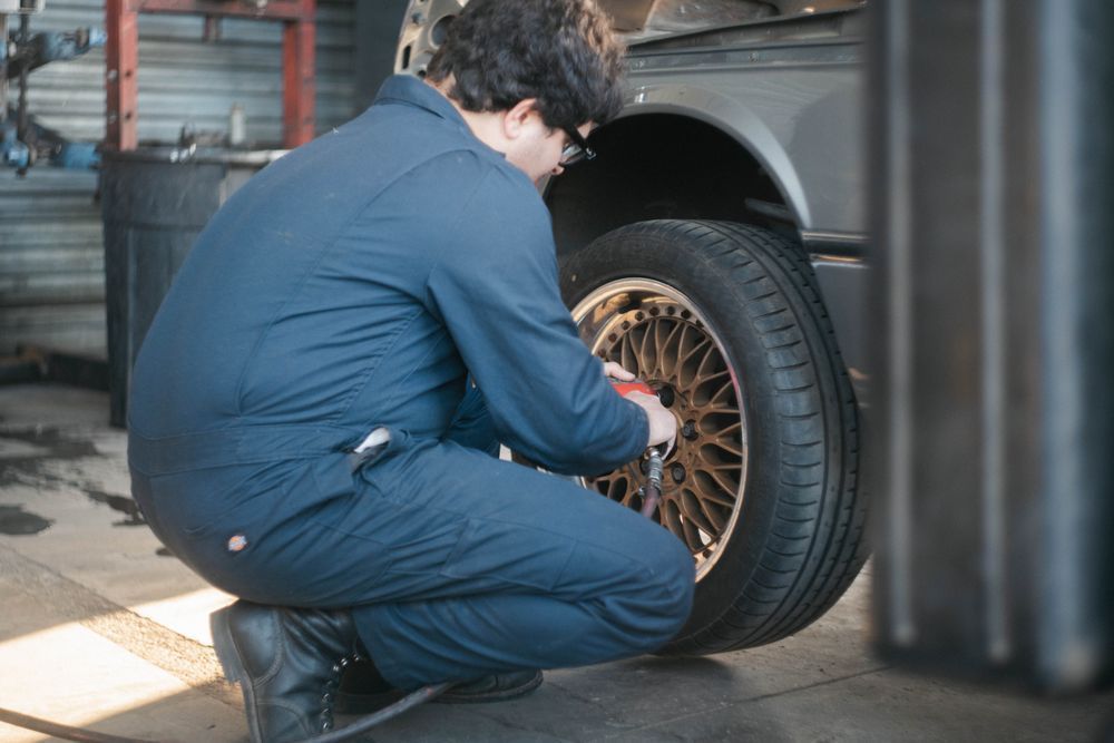 Mechanic kneeling beside a car, inspecting or tightening the front wheel in a garage.