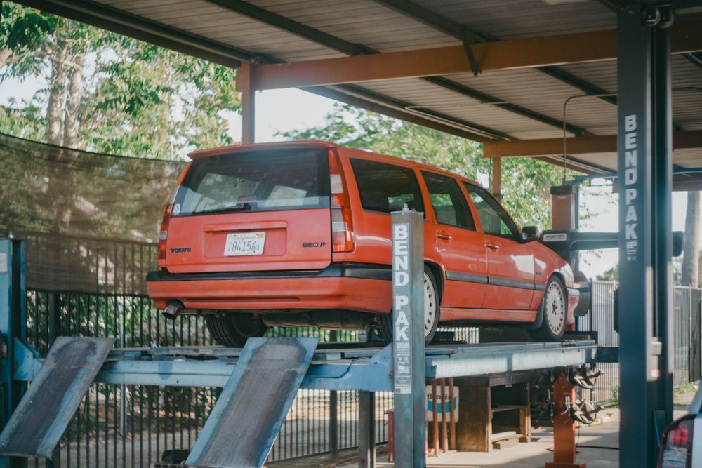 Red hatchback on a car lift in an auto repair shop under a metal roof