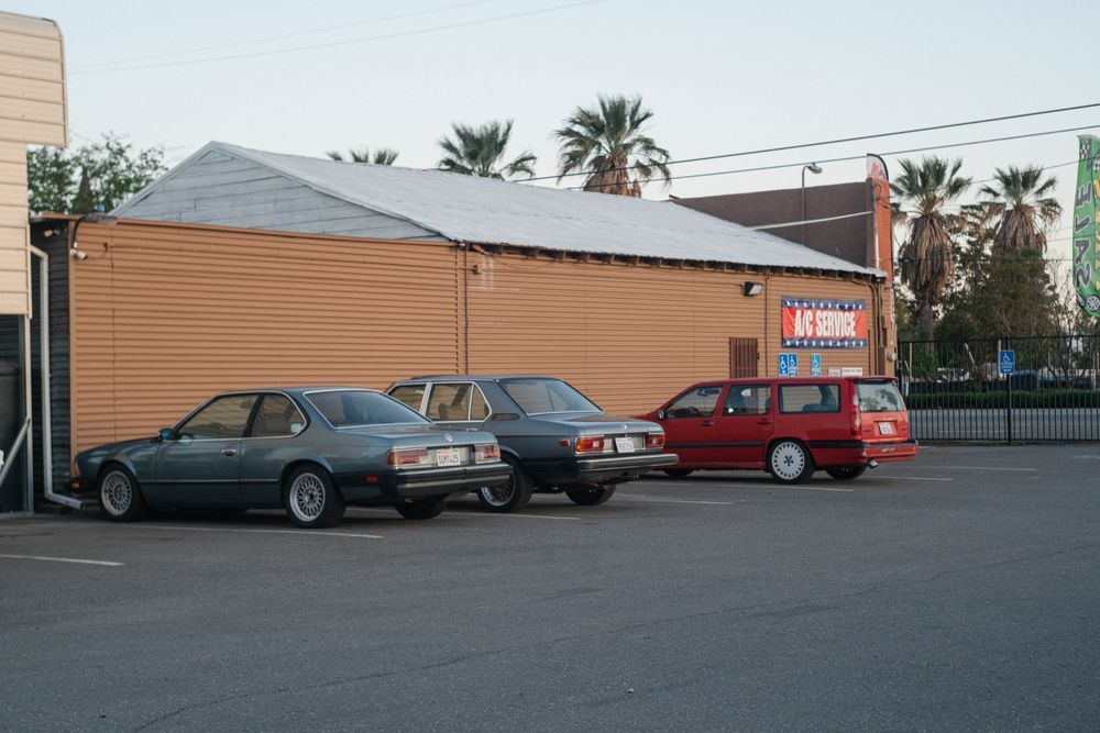 Parked cars beside a tan building with a lit sign at dusk