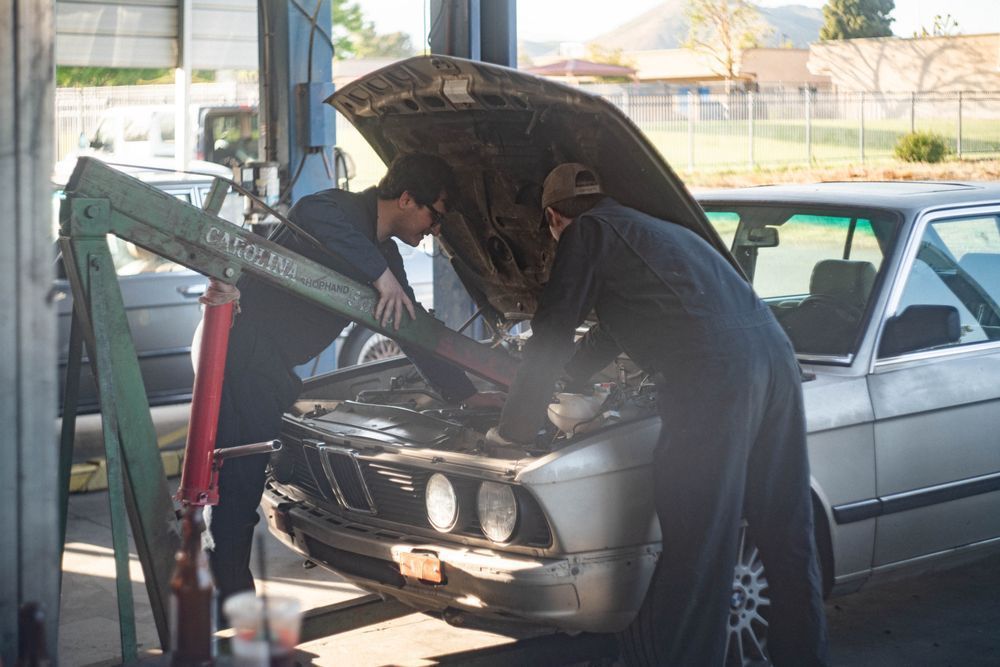 Mechanic working under an open hood of a silver car in a garage