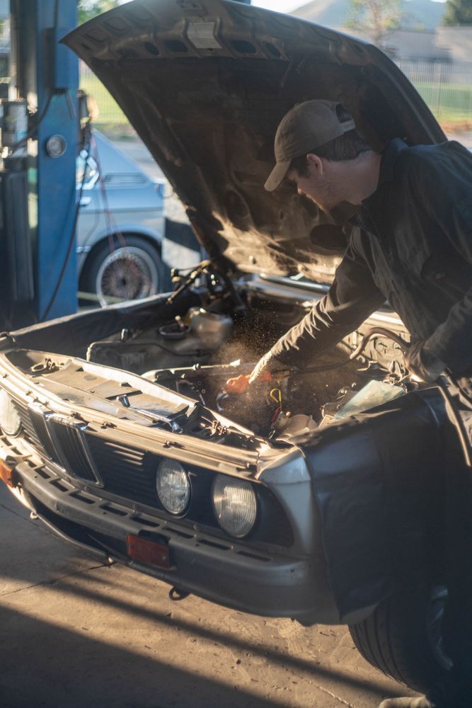 Mechanic welding inside a car’s open engine bay in a garage, sparks flying.