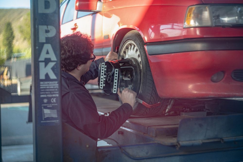 Mechanic using a wheel balancing machine on a red car in a garage