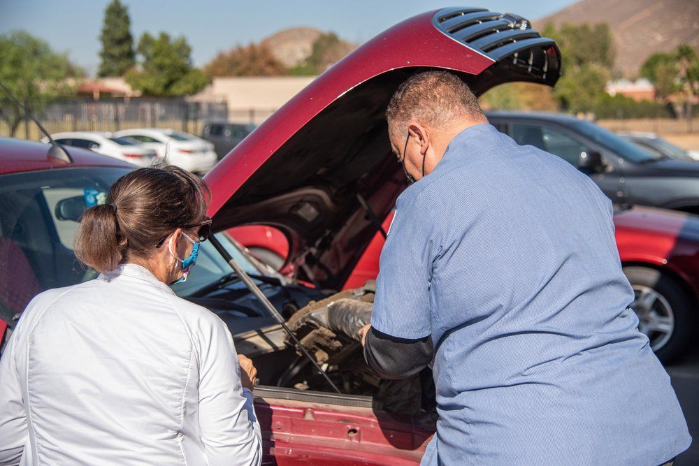 Two people inspecting a red car with its hood open in a parking lot
