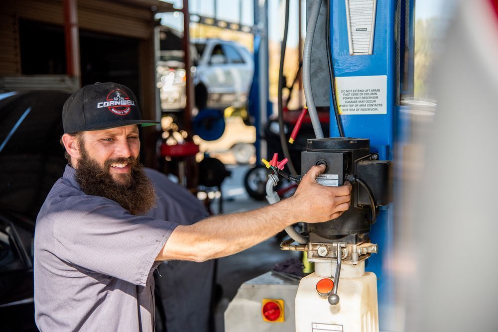 Man in a black cap filling a blue machine with fuel or fluid at a workshop