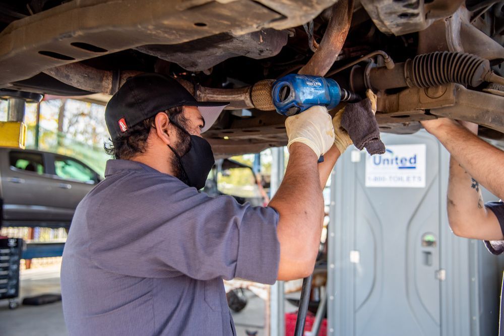 Mechanic using a blue power tool under a vehicle on a lift in an auto repair shop