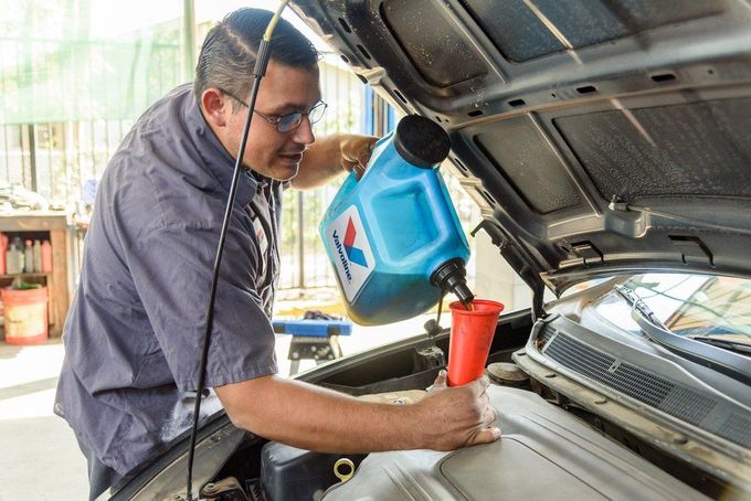 Man pouring blue fluid from a container into a car engine through a red funnel
