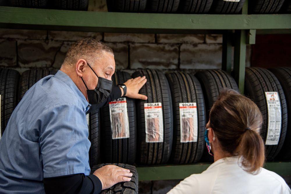 Two people inspect stacked car tires on a shelf in a garage or tire shop.