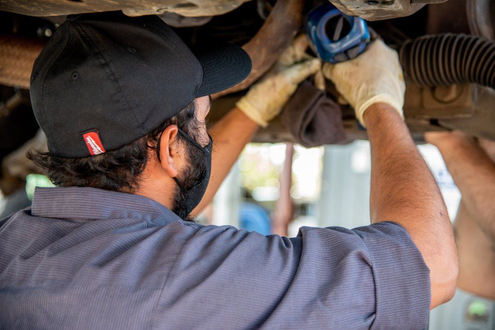 Mechanic wearing gloves inspects the underside of a vehicle with a blue tool